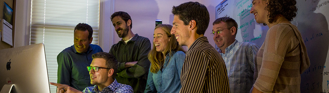 A group of academics gather around a computer to discuss a subject.