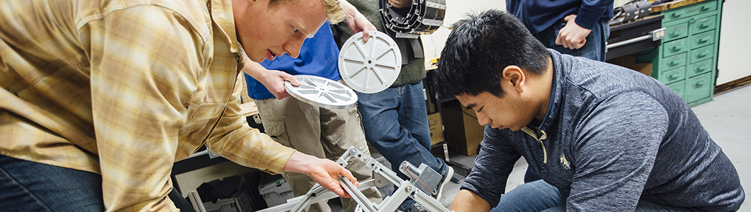 Two students are bent over the skeleton of a rover bound for Mars.