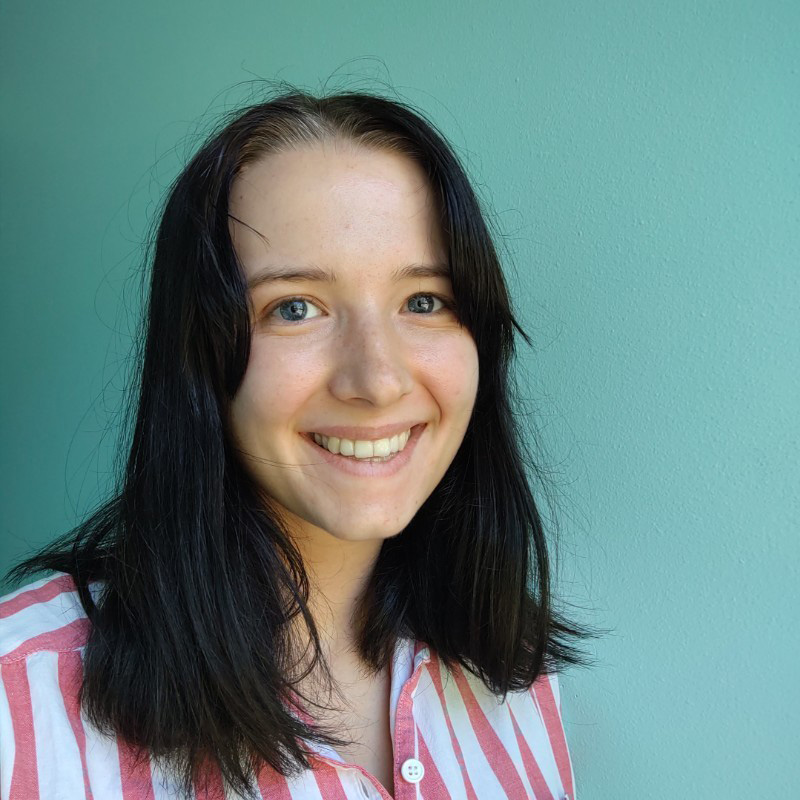 Young woman with black straight hair and blue eyes, smiling and wearing a white and red striped shirt in front of a turquoise background