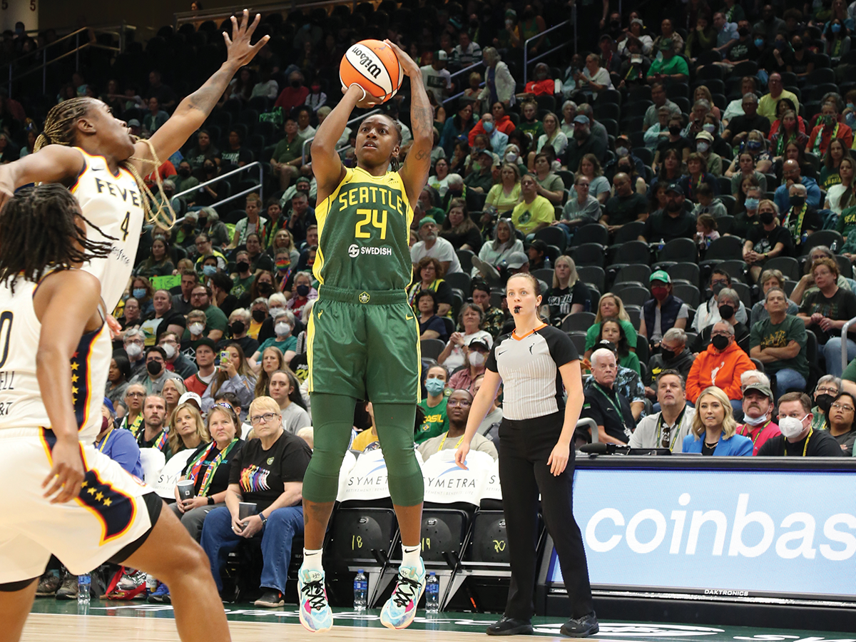 A woman wearing a green and yellow basketball jersey about to shoot the basketball