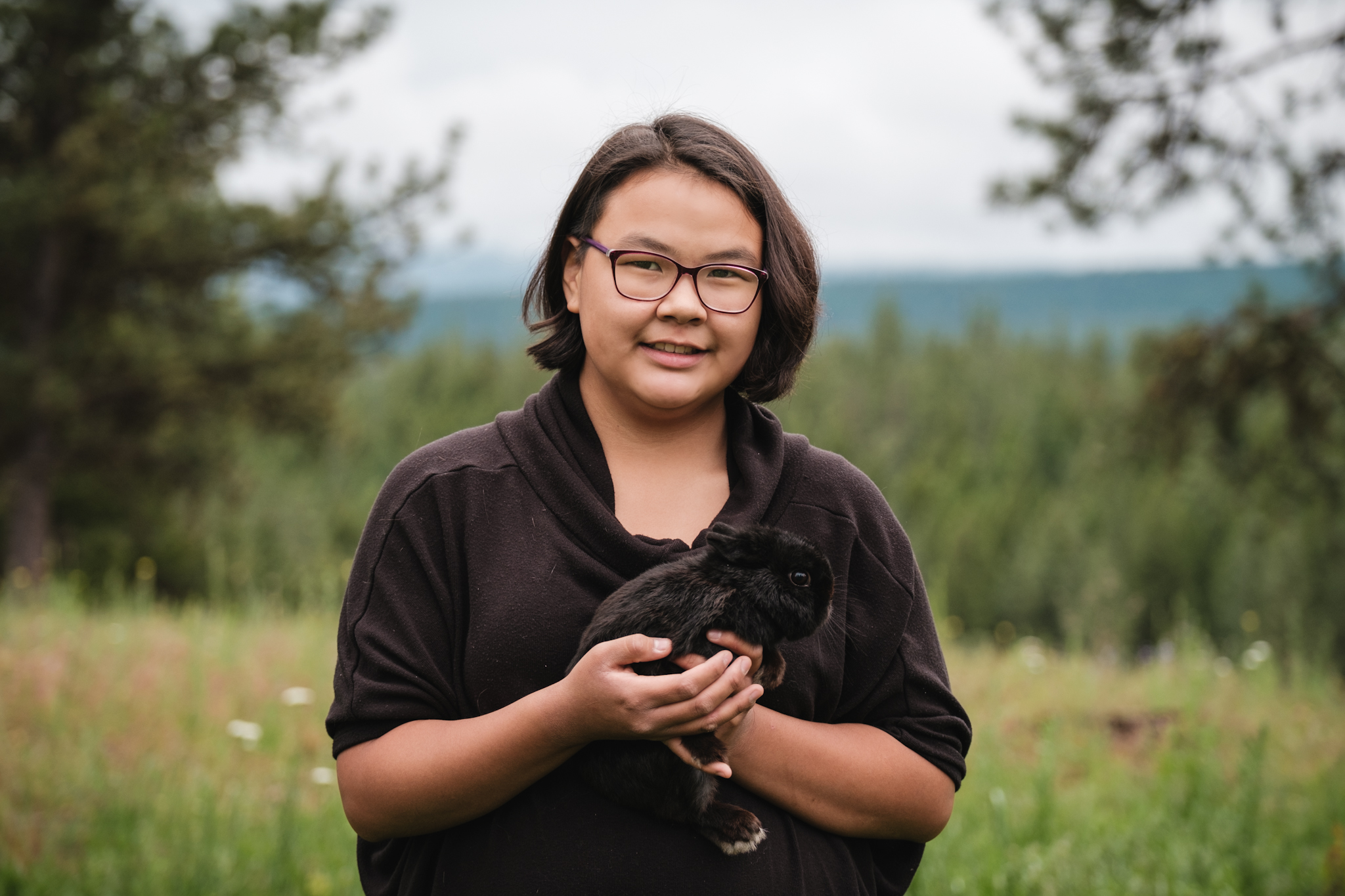 Native American teen holds a black rabbit.