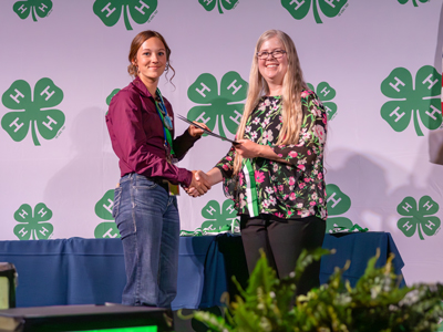 4-H member shaking hands and holding an award at 4-H Congress