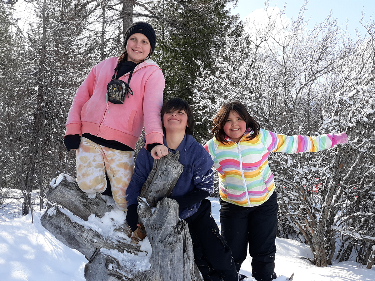 Three young kids posing on a log in the snow