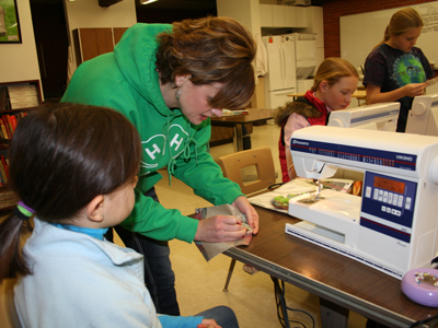 A 4-H member watching a woman sewing