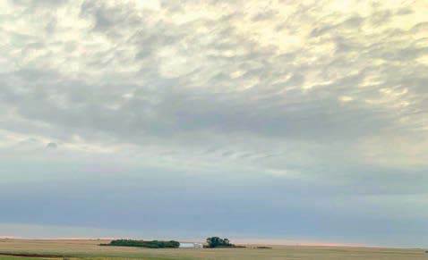 A broad expanse of relatively calm sky with textured cloud formations over open farmland. 
