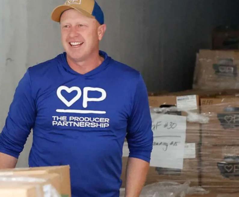 Matt Pierson wears a blue and gold baseball hat and a blue shirt with the Producer Partnership logo on the front