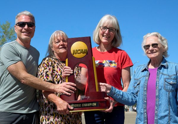 Four people posing outdoors while holding an NCAA FCS National Champion trophy.