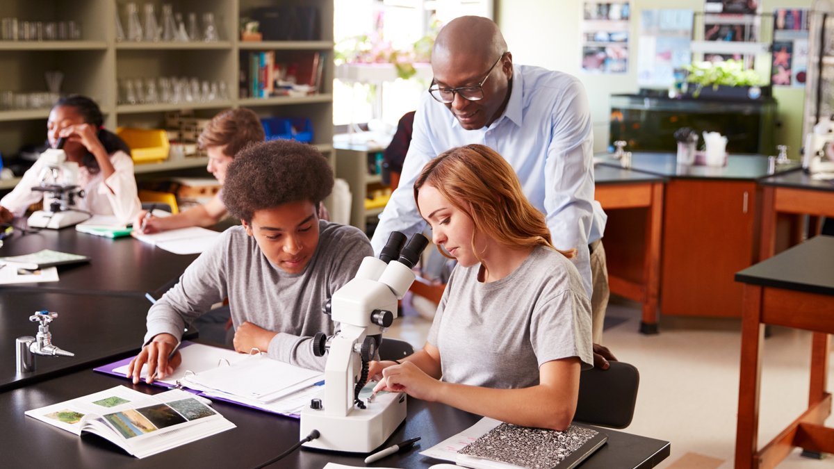 Teacher and two students in front of a microscope
