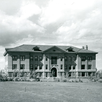 Linfield Hall is a three-story rectangular brick building with concrete footings topped with three gables on the roof, two small gables situated on the outside of one large gable. There are also two chimneys on the right side of the building.