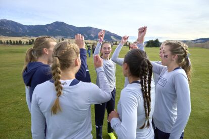 Cross-country team in a huddle raising fists outdoors with mountains in the background.