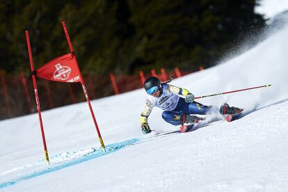 Skier in racing gear sharply turns around a red gate on a snowy slope during a ski race.