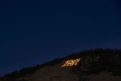 Large illuminated letter M on a hillside under a starry night sky.