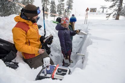 Researchers measure snow depth and collect data in a deep snow pit at a snowy forest site.