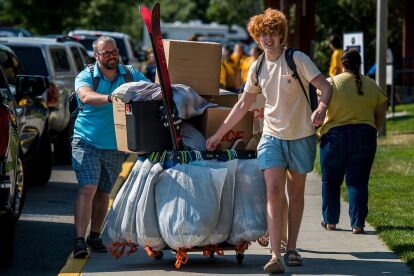 Student and adult push a cart loaded with boxes and bags during move-in day on campus.