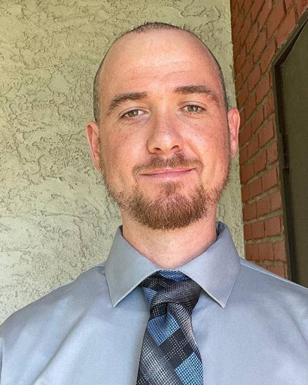 A person with light facial hair wearing a blue collard shirt and a tie