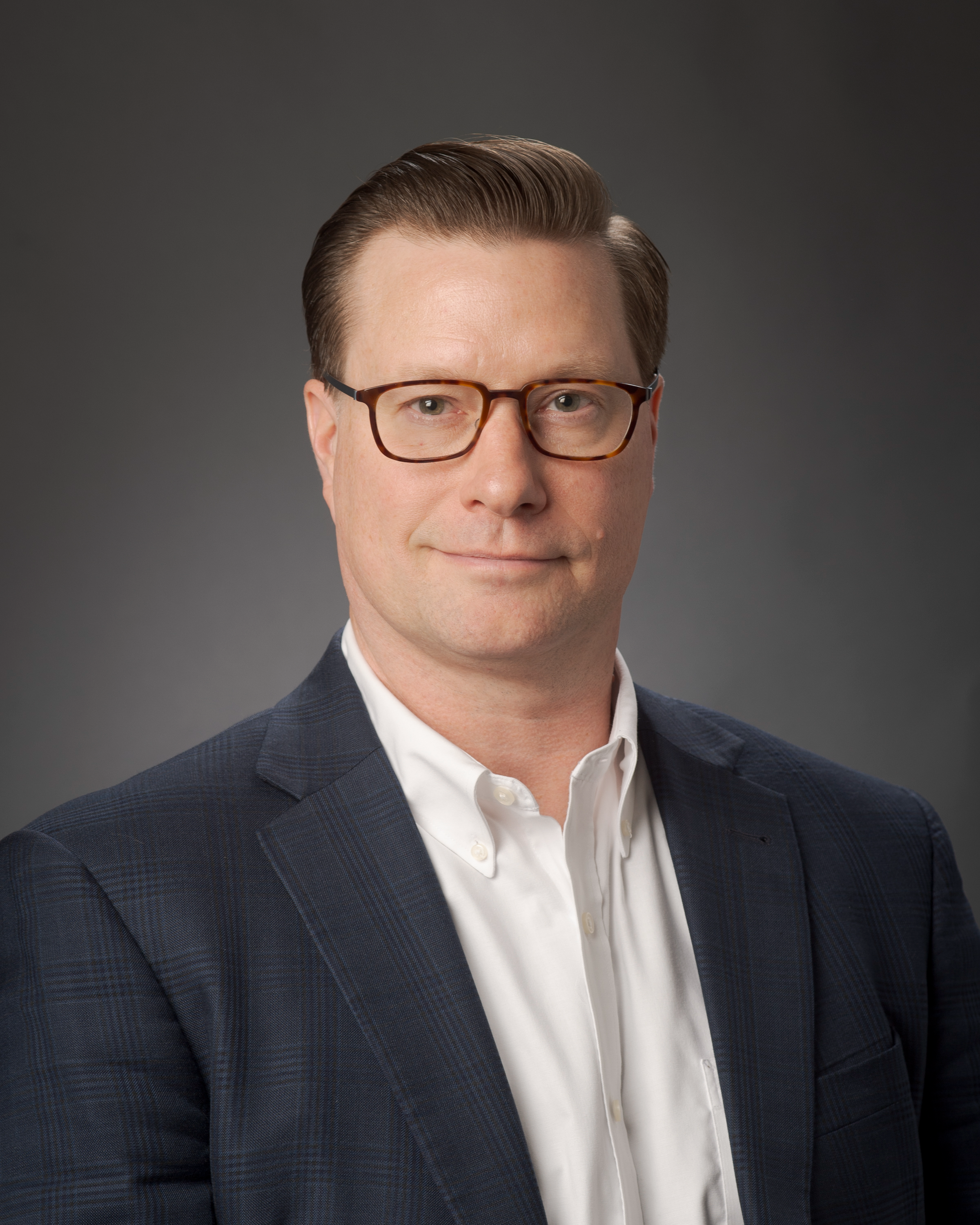 A portait of a man with short brown hair wearing glasses and a suit