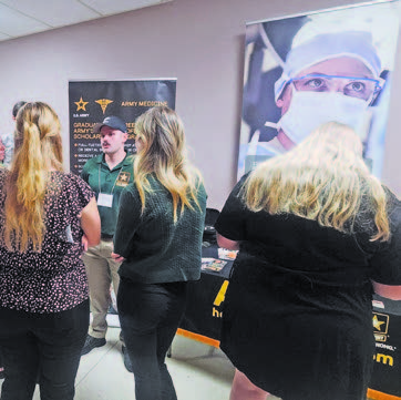 A man standing next to a conference table talking to three women who can only be seen from their backs.