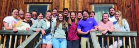 A group of 16 women and men smiling and looking straight ahead. 