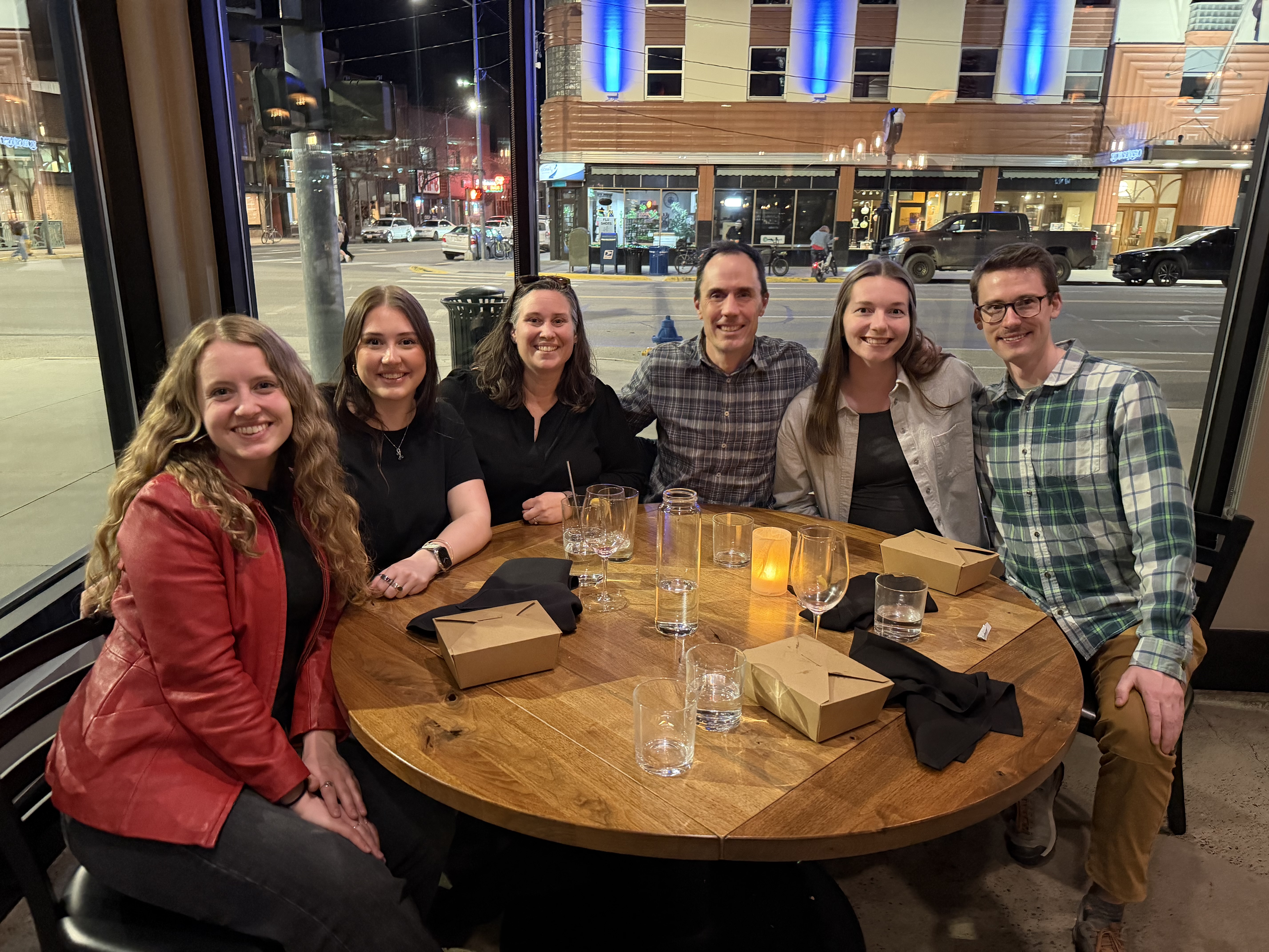 A group of six people sitting around a restaurant table afer dinner. 